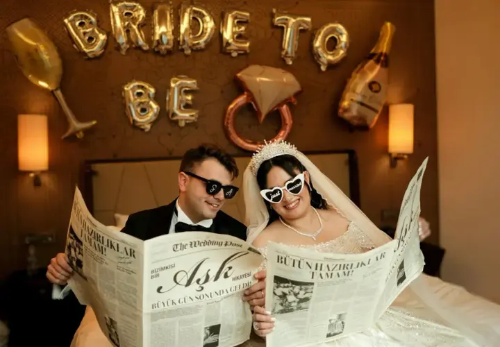 Para Młoda czyta gazetę "The Wedding Post" o miłości, przygotowując się do wesela krok po kroku. Balony "Bride to Be" i kieliszki tworzą atmosferę.