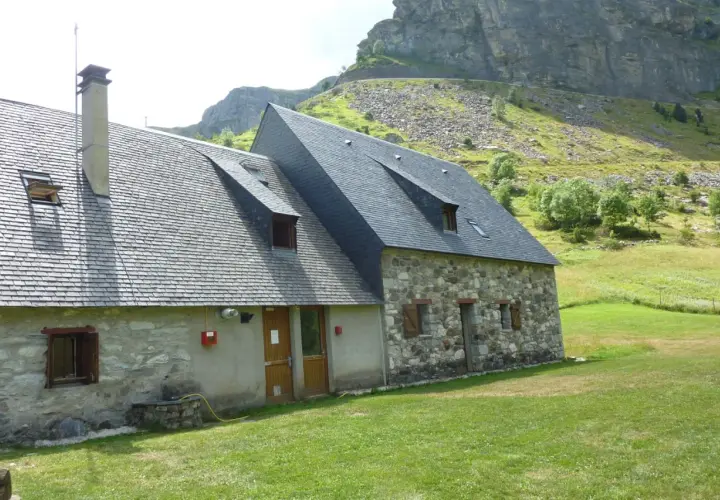 El refugio Vignemale, una construcción de piedra y pizarra, se alza en un prado verde bajo imponentes montañas rocosas.