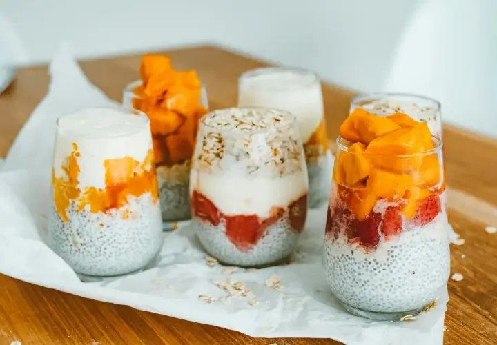 Sześć deserów z nasion chia, jogurtu i owoców (truskawki, mango) w szklankach.