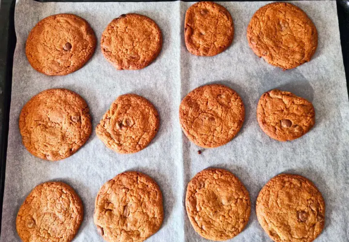 Nybakade chocolate chip cookies på bakplåtspapper. Perfekt för ett enkelt recept!