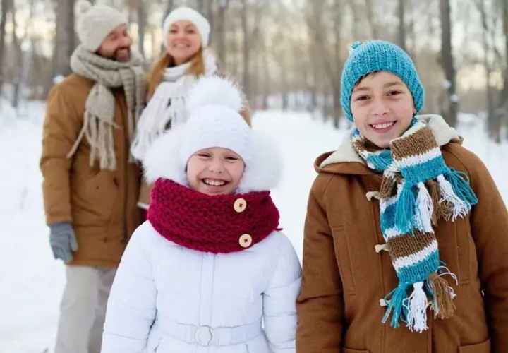 Familia sonriendo en un día de **invierno para niños**. Los niños al frente llevan abrigos y bufandas coloridas.