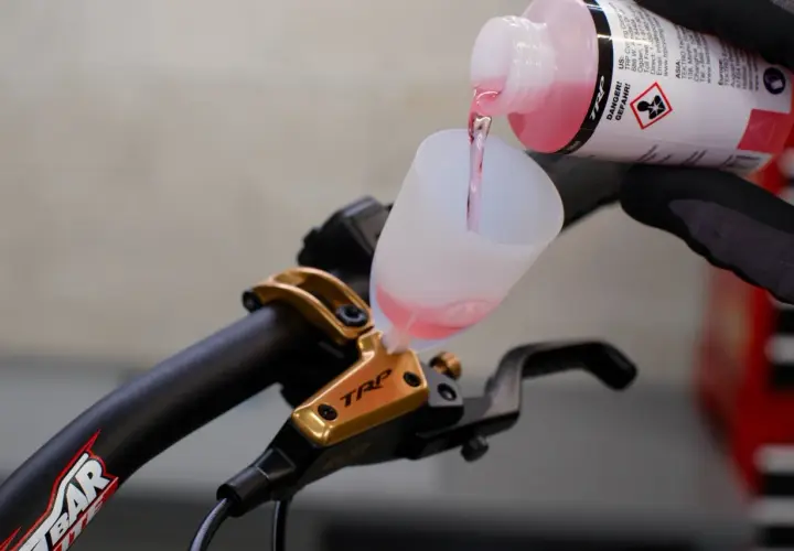 Adding brake fluid without bleeding is not recommended. This image shows pink fluid being poured into a funnel on a TRP brake lever.