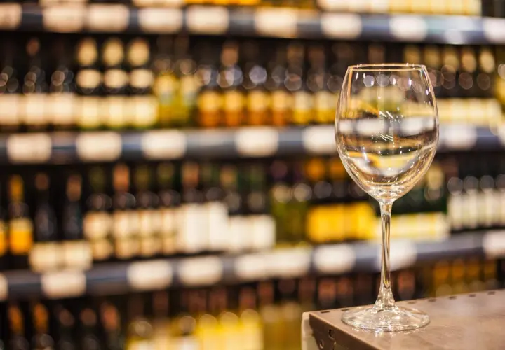 Verre à vin vide sur un comptoir, devant des étagères remplies de bouteilles. L'ambiance évoque une dégustation de vin à Paris.