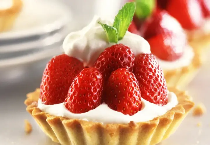 Deliziosi dolci con fragole fresche e panna montata, guarniti con una fogliolina di menta.