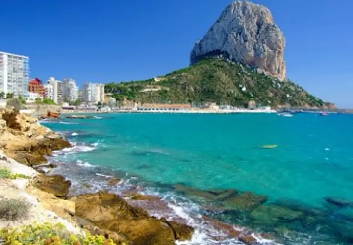 Vista del natural park of Penyal d'Ifac con aguas turquesas, rocas y edificios costeros.