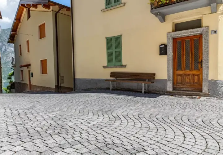 Pavimentazione in pietra per esterni carrabili, con case color pastello e un panchina.