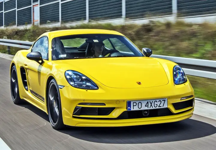 Żółty Porsche Cayman T pędzi po drodze, kierowca w czapce z daszkiem za kierownicą.