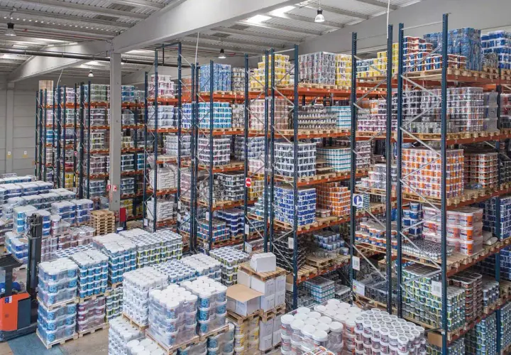 Großes Lager mit vielen Regalen voller Farbeimer und anderer Arbeitsmittel. Ein Gabelstapler steht bereit.