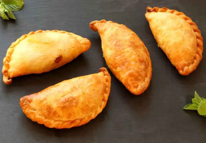 Cuatro empanadillas doradas y crujientes, recién hechas en freidora de aire, reposan sobre una pizarra oscura.