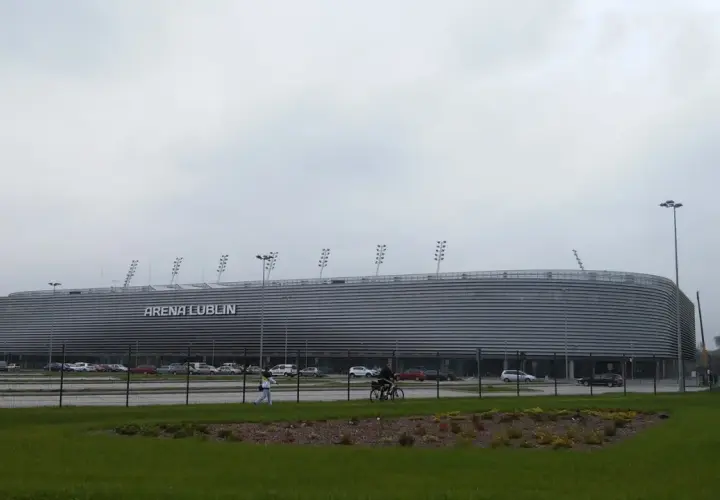 Nowoczesny stadion Arena Lublin z charakterystyczną, falistą fasadą. W tle parking i niebo.