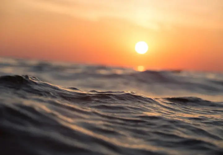 Olas suaves reflejan el atardecer anaranjado. Es como soñar con agua de mar, una paz que te envuelve.