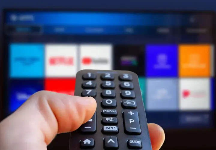 Hand håller fjärrkontroll framför en TV-skärm med app-ikoner. Kanske dags att välja en film eller en dokumentär om ze rappare.