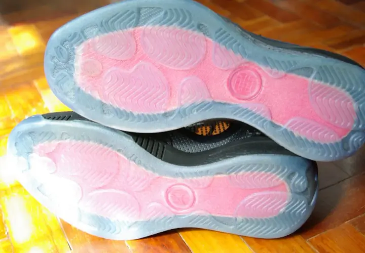 Soles of two black sneakers with pink grip zones and clear rubber outsoles. These shoes are designed to maximize traction, offering a great solution for how to make shoes more grippy.