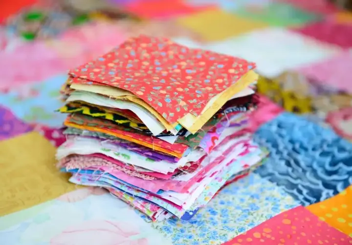 Stos kolorowych kwadratów materiałów, gotowych do stworzenia patchworku. To właśnie patchwork – sztuka łączenia skrawków tkanin w piękne wzory.