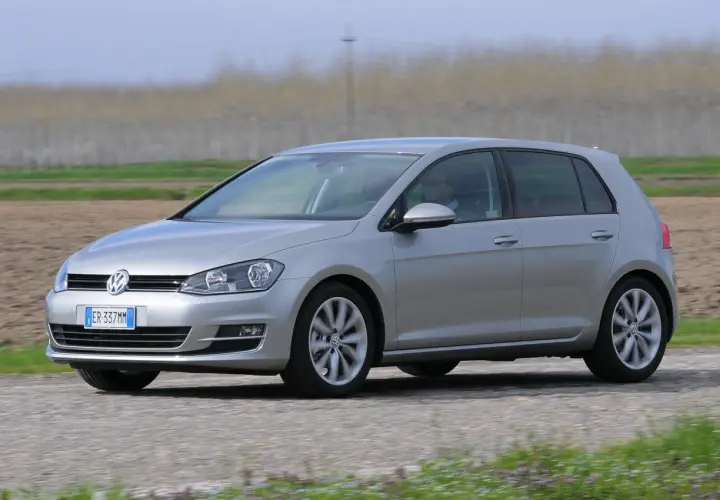 Volkswagen Golf 1.6 TDI argento in movimento su strada sterrata, con campi coltivati sullo sfondo.