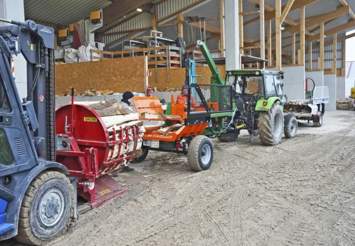 Holzspalter und Traktor mit Anhänger, bereit für den Transport. Die mobilen Förderbänder sind im Einsatz, um das Holz zu bewegen.