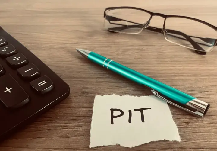 Kalkulator, zielony długopis i okulary leżą obok kartki z napisem PIT. Czas rozliczyć PIT 36L.