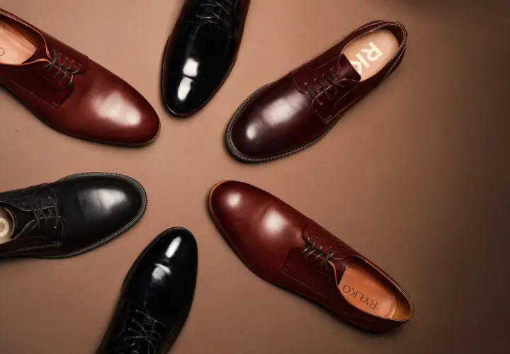 Eleganckie brązowe buty do czarnego garnituru i czarne lakierki, obie pary od Ryłko, ułożone na brązowym tle.