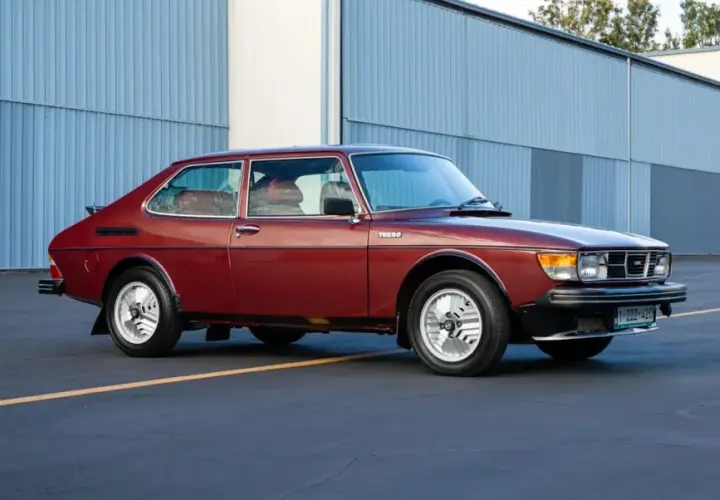 En röd Saab 99 Turbo står parkerad framför en blå hangar.