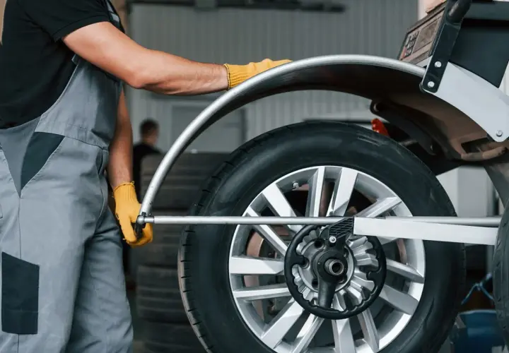 Mechanik w żółtych rękawiczkach ustawia koło na wyważarce. Dowiedz się, ile kosztuje wyważenie kół.
