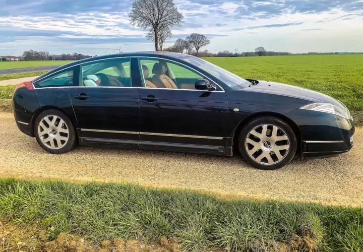 Ciemny Citroën C6 z beżowym wnętrzem stoi na żwirowej drodze obok zielonego pola.