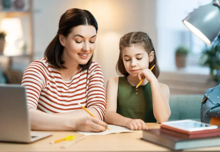 Mama pomaga córce w nauczaniu domowym podstawówka. Razem piszą w zeszycie, obok leży laptop.
