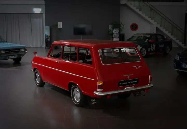 Röd Opel Kadett Caravan, en klassiker som kan vara en skattebefriad bil. Bredvid står en blå bil och en racingbil.