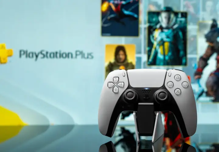 Biały kontroler DualSense na tle ekranu z logo PlayStation Plus i okładkami gier. Idealny do grania w gry z oferty PS Plus marzec.