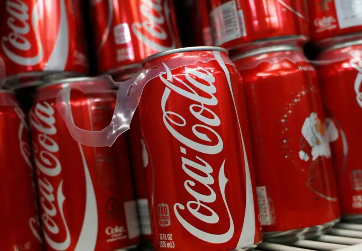 Puszki Coca-Coli ułożone na półce, jedna z nich z widoczną etykietą kaloryczną.