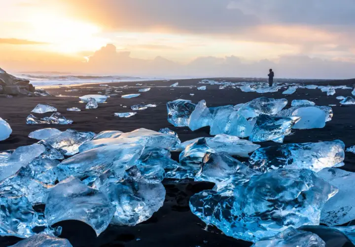 Fragmentos de hielo brillan en la arena negra del Diamond Beach de Islandia, bajo un cielo crepuscular.