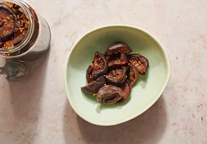 A jar and bowl of glistening pickled shiitake mushrooms, studded with mustard seeds.