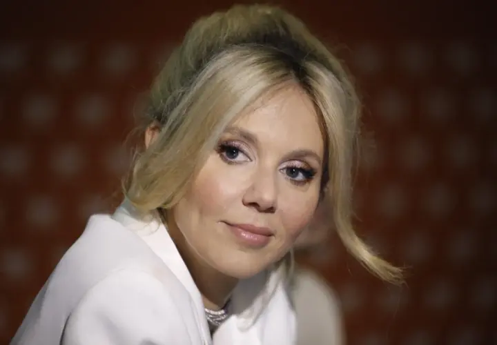 Kasia Moś, której wiek dodaje jej uroku, w białej marynarce z błyszczącym naszyjnikiem.