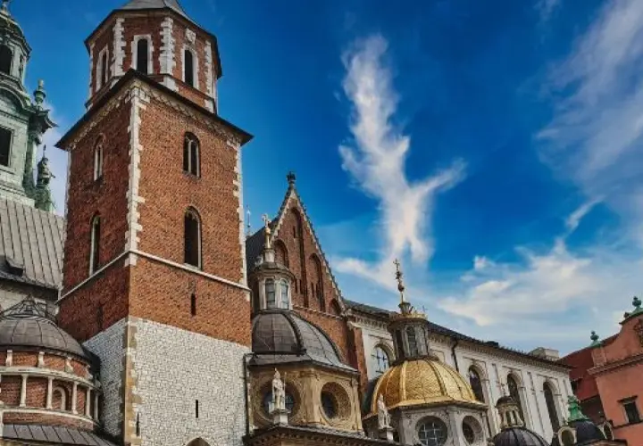 Kraków: Wawel z ceglaną wieżą, złotą kopułą i zielonym dachem pod błękitnym niebem.