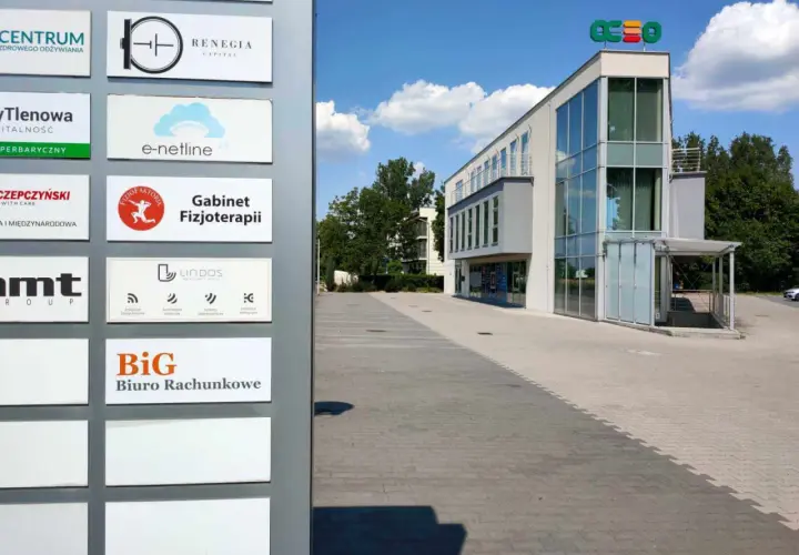 Tablica z nazwami firm, w tym "BiG Biuro Rachunkowe", przed nowoczesnym budynkiem biurowym.