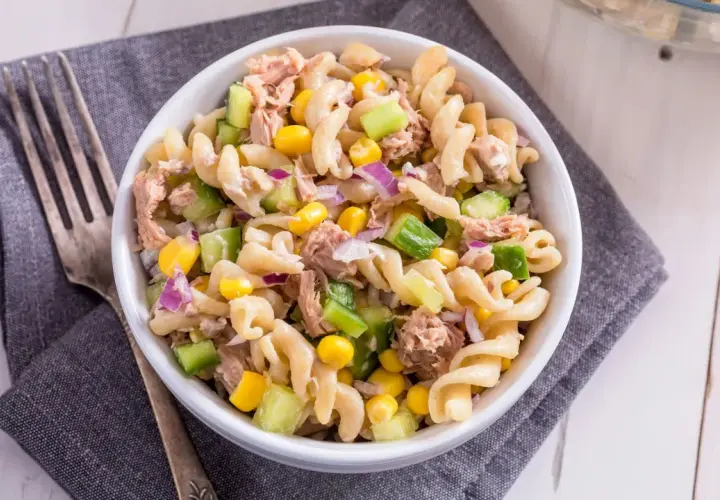 Ein köstlicher nudelsalat mit thunfisch, garniert mit Mais, Gurken und roten Zwiebeln, bereit zum Genießen.