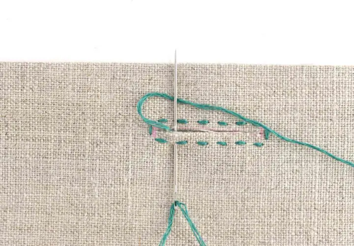 Close-up of a needle and teal thread being used to sew a buttonhole on beige fabric. Stitches are visible along the edges of the cut.