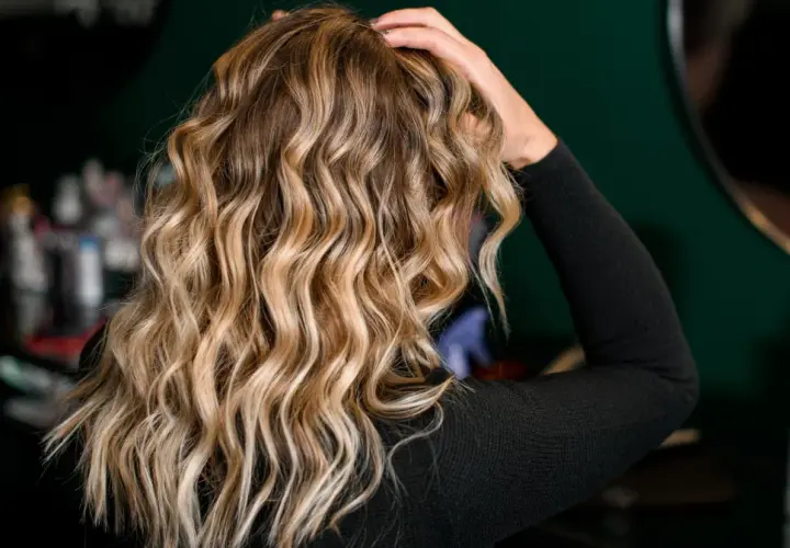 Blond włosy z falami, ułożone z pomocą aktywatora skrętu. W tle kosmetyki fryzjerskie.