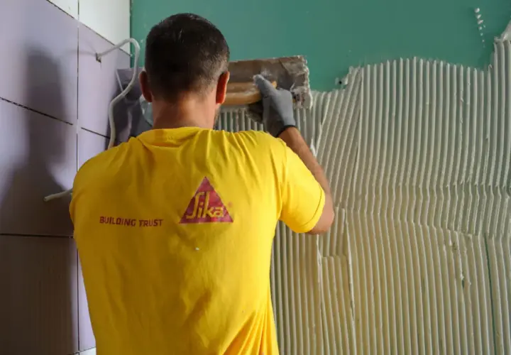 Operaio con maglia gialla Sika applica colla per la partenza posa piastrelle a muro.