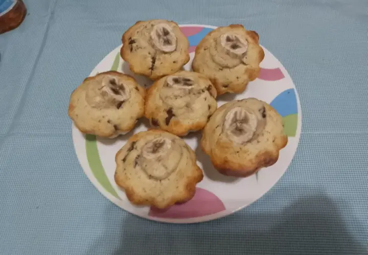 Sei muffin banana e cioccolato, guarniti con una fetta di banana, su un piatto colorato.