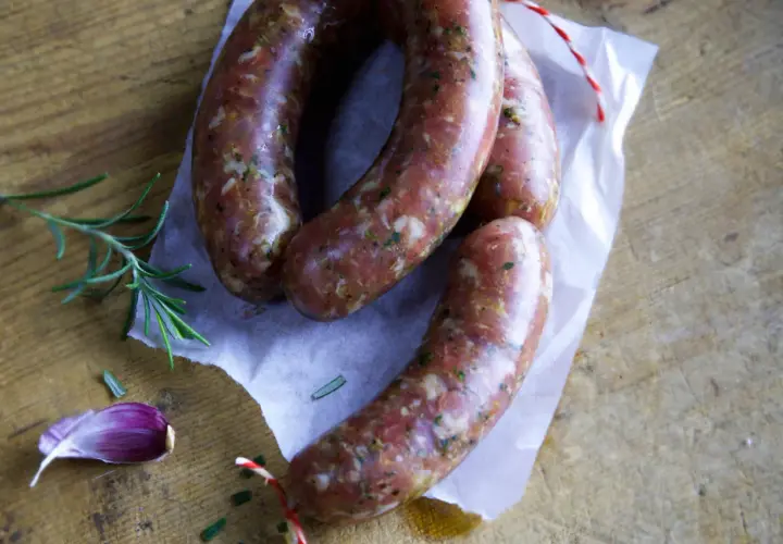 Frische italienische Bratwurst Salsiccia, bereit für ein köstliches Rezept. Rosmarin und Knoblauch liegen daneben.