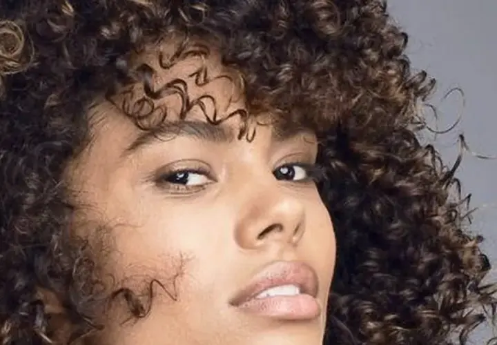 Mujer con cabello rizado y oscuro, mostrando cómo nutrir el pelo para un brillo saludable.