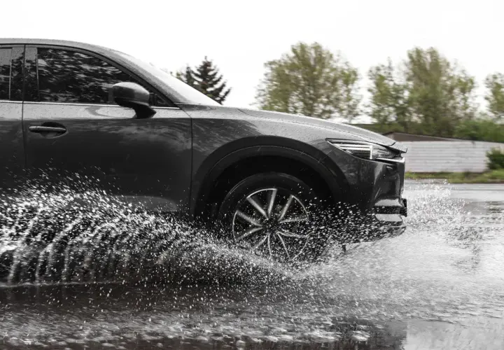 Ciemny samochód na mokrej drodze, koło rozpryskuje wodę, groźny aquaplaning.