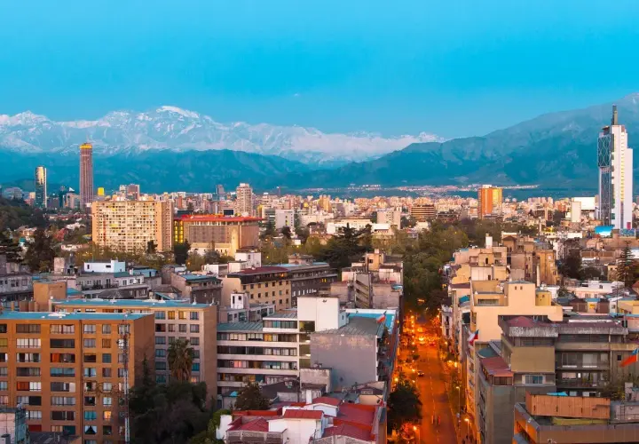 Widok na Santiago, stolicę Chile, z górami w tle. Miasto tętni życiem, a światła uliczne rozświetlają wieczór.