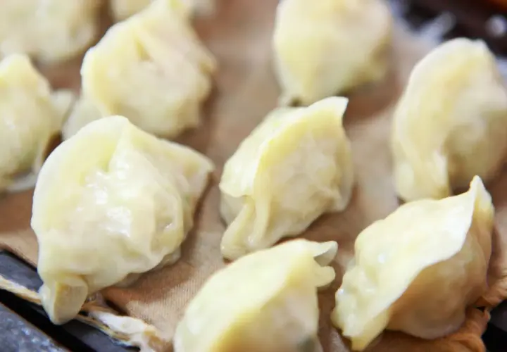 Parowane pierożki dim sum, delikatnie ułożone na brązowym papierze, kuszą swoim wyglądem.