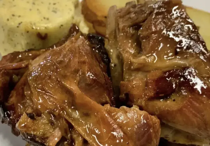 Succulento agnello al forno, dorato e lucido, servito con patate arrosto e una cremosa salsa verde.