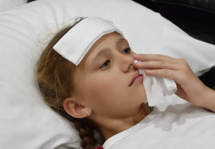Bambina con impacco sulla fronte e fazzoletto per fermare il sangue dal naso.