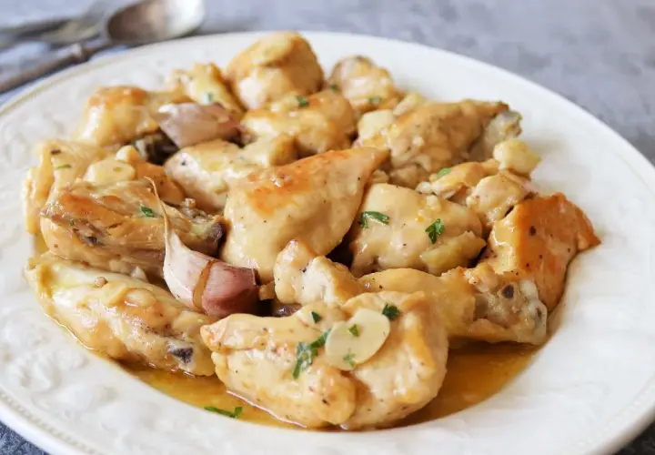 Sabroso pollo al ajillo servido en un plato blanco, con trozos de pollo dorados y jugosos, cubiertos con una salsa de ajo y perejil.