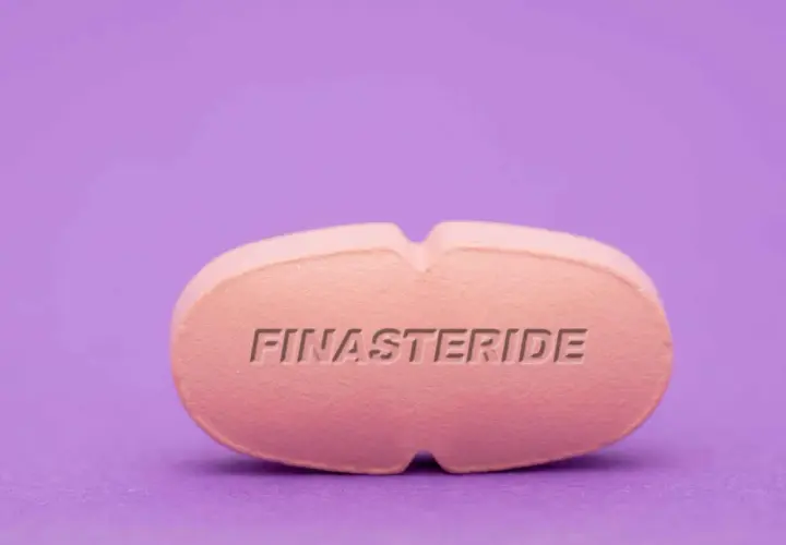Różowa tabletka z napisem FINASTERIDE na fioletowym tle.