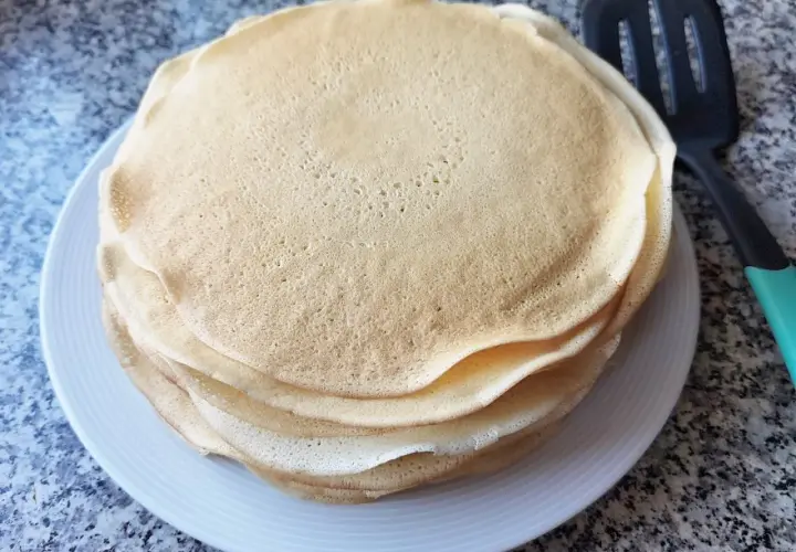 Stos cienkich, złotych placków, idealne ciasto na krokiety, leży na białym talerzu obok łopatki.