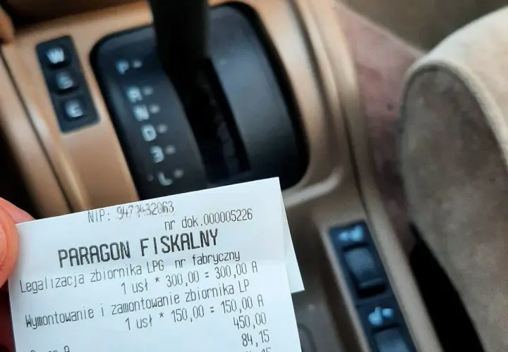 Paragon fiskalny za legalizację i montaż zbiornika LPG na tle deski rozdzielczej samochodu.